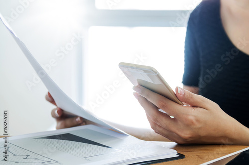 Business, office concept. Woman holding mobile and financial document at her desk.