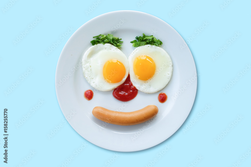 Smiling face frying eggs breakfast on a plate isolated white blue background. Smiling face frying eggs breakfast on a plate isolated white blue background.