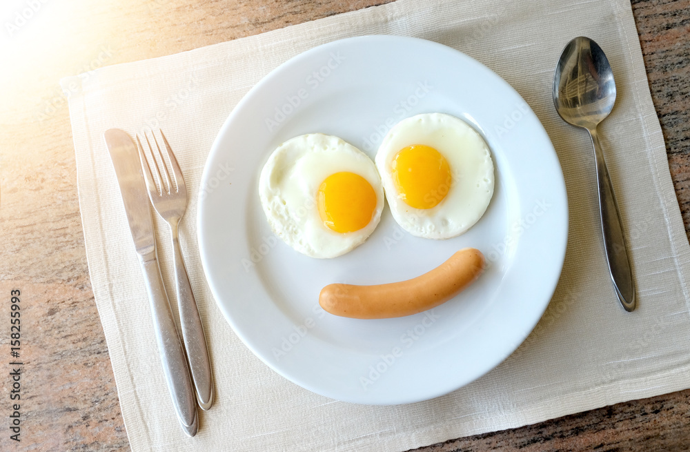 Smiling face frying eggs breakfast on a white plate background with knife and fork on a fabric table, breakfast serve for kid. Smiling face frying eggs breakfast on a white plate background with knife and fork on a fabric table, breakfast serve for kid.
