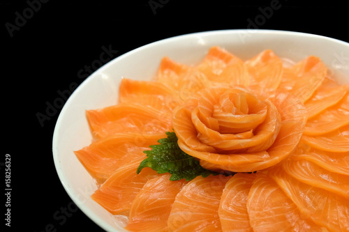 Salmon sashimi serve on flower shape on ice white bowl boat on black isolated background.