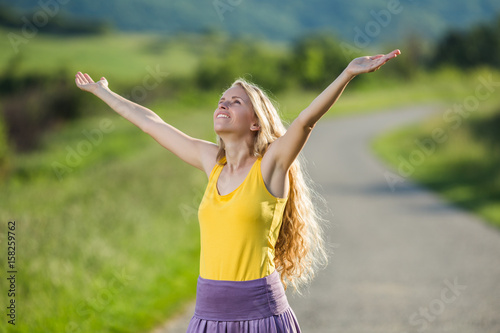 Happy woman standing at the country road with her arms raised.