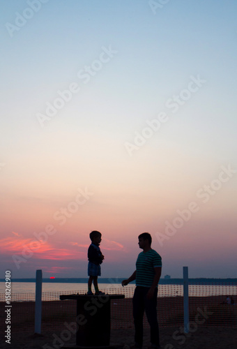 Silhouettes of a father and son at sunset at the sea shore