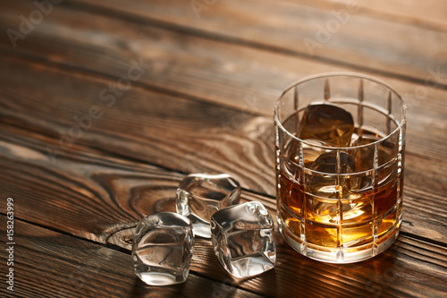 Glass of whiskey with ice cubes on wooden table © haveseen