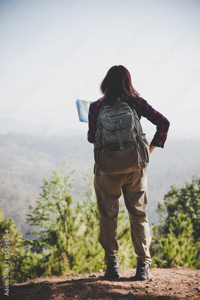 Young woman standing on the peak on mountain watching on map.