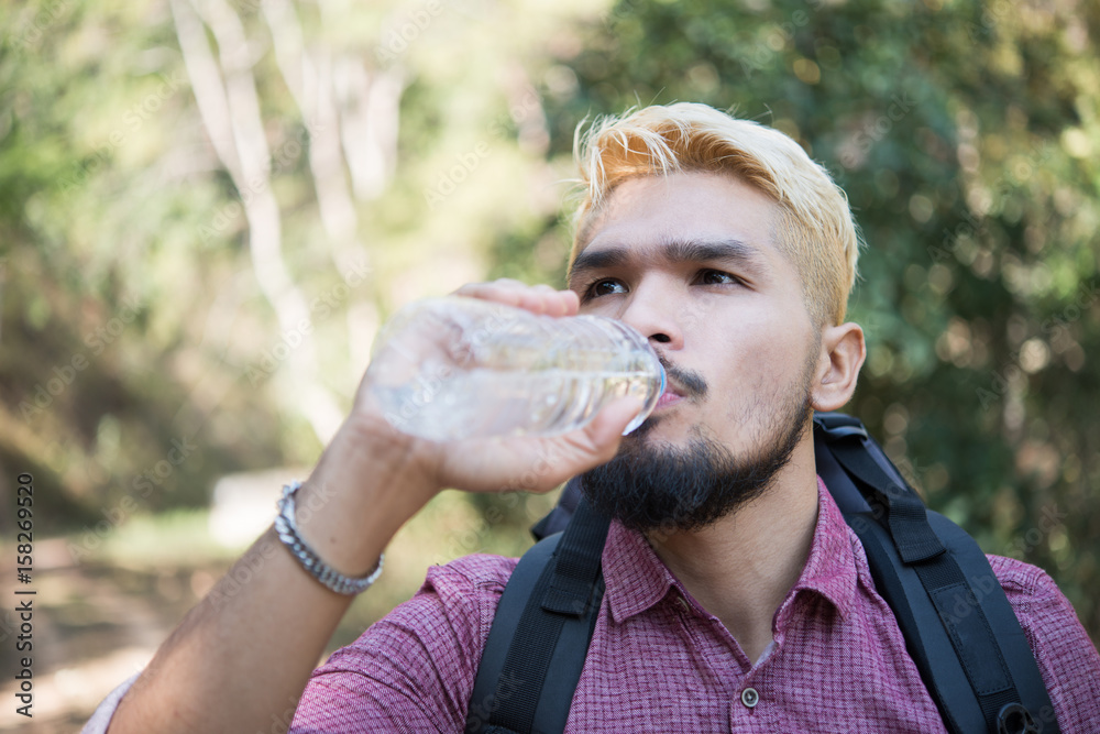 Obraz premium Hiker man drinking water in forest on mountain.