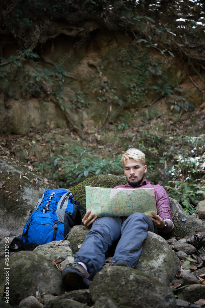 Young attractive man sitting in the forest and resting during hiking.