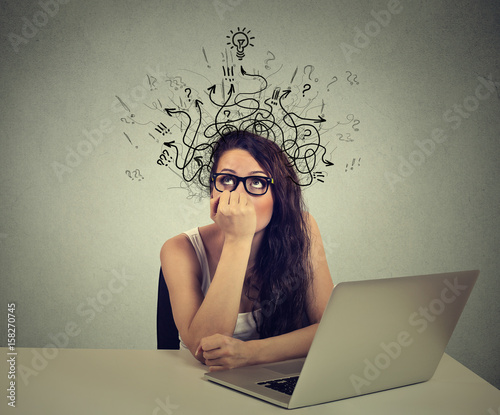 woman with thoughtful expression sitting at a desk with laptop with arrows and symbols coming out of head photo