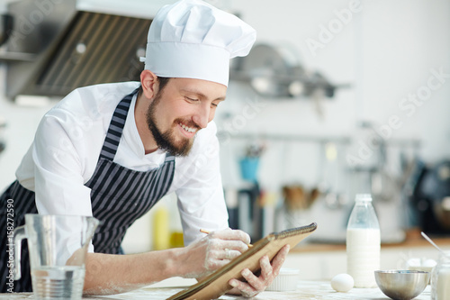 Happy chef writing something in notepad over workplace