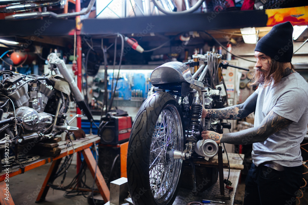 Side view portrait of tattooed man working in garage repairing big motorcycle Side view portrait of tattooed man working in garage repairing big motorcycle