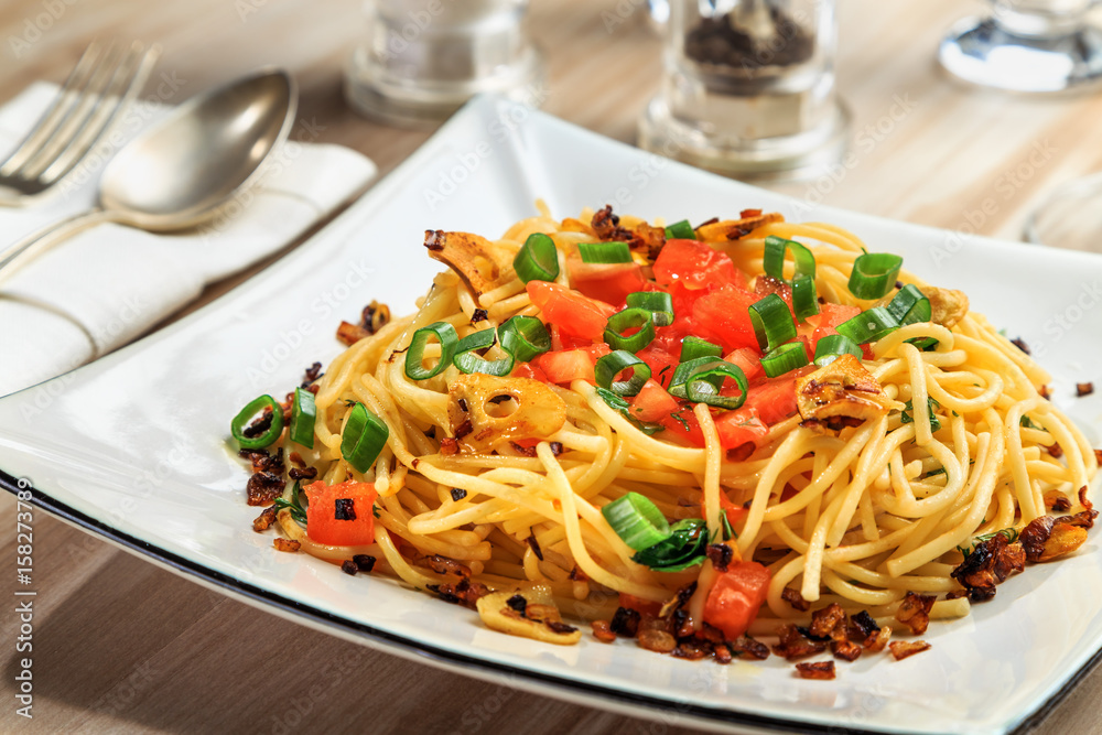 spaghetti with tomatoes, roasted garlic and green onions on a beautiful rectangular plate are on the table