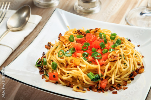 spaghetti with tomatoes, roasted garlic and green onions on a beautiful rectangular plate are on the table