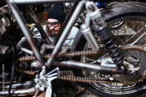 Portrait of brutal bearded man assembling custom motorcycle in garage