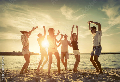 Friends funny dance on the beach under sunset sunlight.
