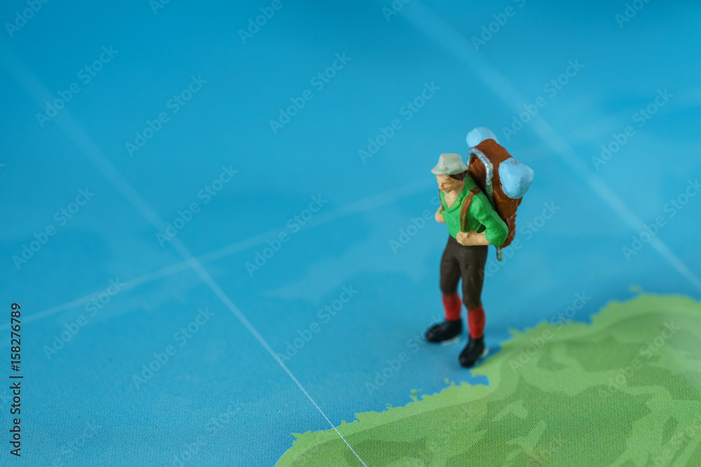 Travel concept as a miniature figure with backpack walking on map with green coastal and blue sea Travel concept as a miniature figure with backpack walking on map with green coastal and blue sea