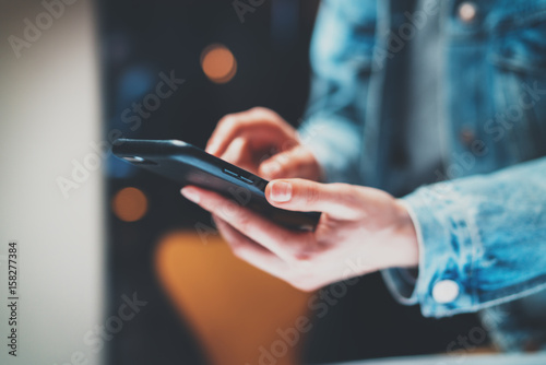 Closeup view of female hands holding modern smart phone and pointing fingers on the touch screen at night.Horizontal, blurred background, bokeh effects.