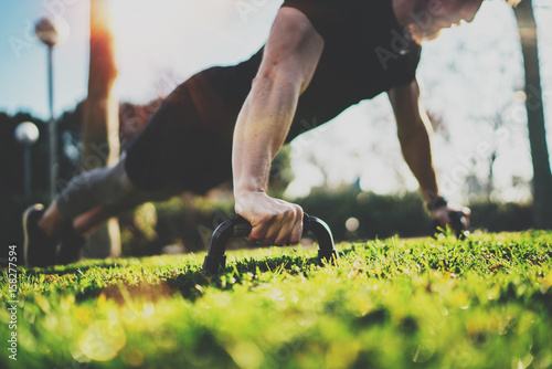 Healthy lifestyle concept.Functional training outdoors.Handsome sport athlete man doing pushups in the park on the sunny morning. Blurred background.Horizontal.Flares,sunlight effect.