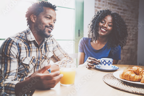 Happy african american couple are having breakfast together in the morning at the wooden table.Young black man and his girlfriend drinking fresh juice and black coffee on breakfast at at home.