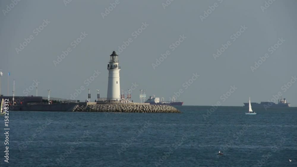 Sailboat sailing in sea,relying on lighthouse dam.water surface. Sailboat sailing in sea,relying on lighthouse dam.water surface.