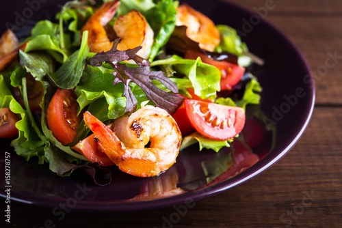 Fresh salad plate with shrimp, tomato and mixed greens (arugula, mesclun, mache) on wooden background close up. Healthy food. Clean eating.