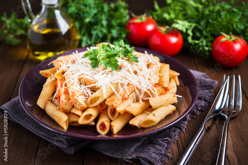 Penne pasta with chicken, tomato sauce, parmesan cheese and parsley on dark wooden background close up. Italian cuisine.
