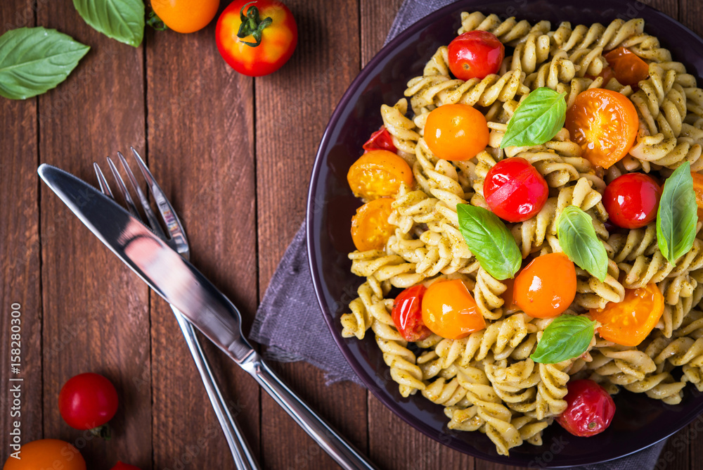 Fusilli pasta salad with pesto genovese, colorful tomatoes and basil leaves on dark wooden background top view. Italian cuisine. Delicious meal. Fusilli pasta salad with pesto genovese, colorful tomatoes and basil leaves on dark wooden background top view. Italian cuisine. Delicious meal.