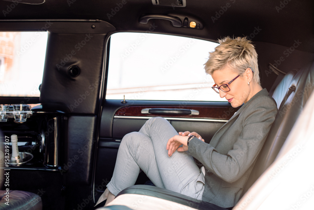 Business woman looking at watch in limousine