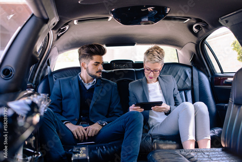 Businesswoman and businessman looking at tablet in limo