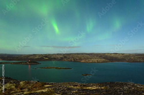 The Aurora in the sky above the hills and water on a moonlit night.