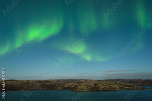 The Aurora in the sky above the hills and water on a moonlit night.