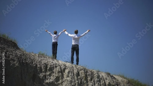 Father and son stand on the top of the hill and satisfied raised their hands to the sky celebrating the victory, free and happy, family celebration, the chaste example for Father's Day