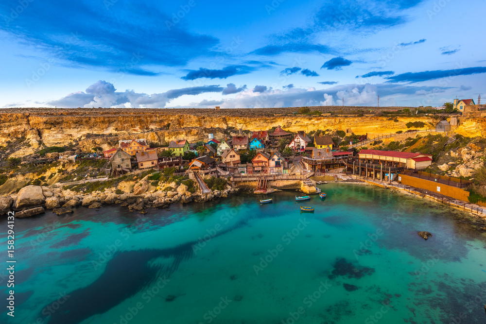 Mellieha, Malta - The famous Popeye Village at Anchor Bay at sunset with amazing colorful clouds and sky
