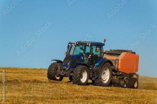 Blue tractor collects dry hay. Agricultural work on the farm in the Czech Republic.