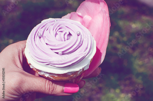 Woman holding pretty pink cupcake in hands with pink flower petals symbolic of Spring cupcakes and dessert