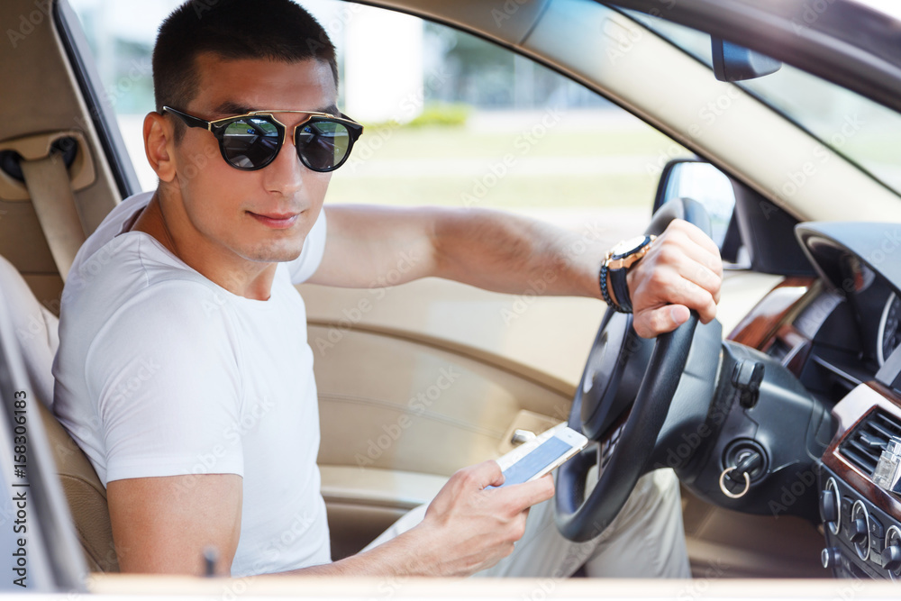Naklejka premium Confident young rich man setting his smart phone and looking at camera while sitting in the car.