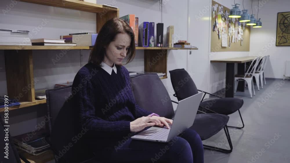 Young woman texting on a laptop on her knees in the office Young woman texting on a laptop on her knees in the office
