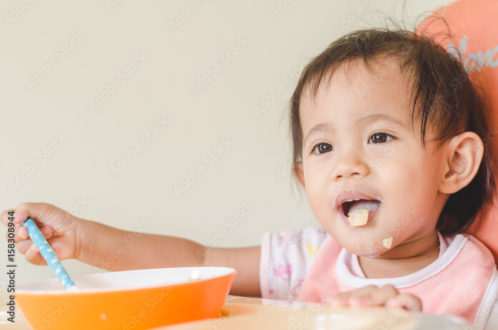 Asian toddler girl eating cereals with milk on high chair at home Asian toddler girl eating cereals with milk on high chair at home