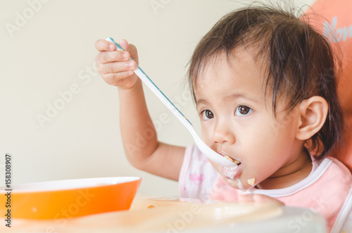 Asian toddler girl eating cereals with milk on high chair at home