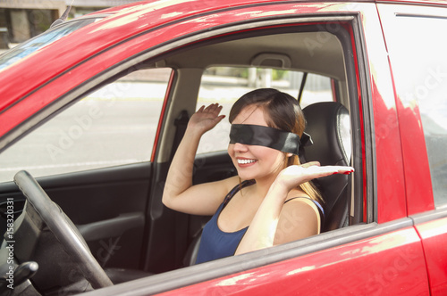 Beautiful smiling young lady with a black rag covered her eyes, while the car drives by itself