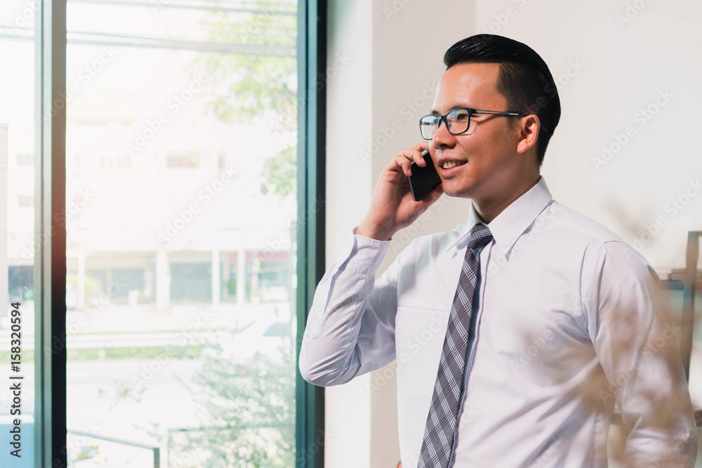Asian Business man using smart phone on window in home office background Asian Business man using smart phone on window in home office background