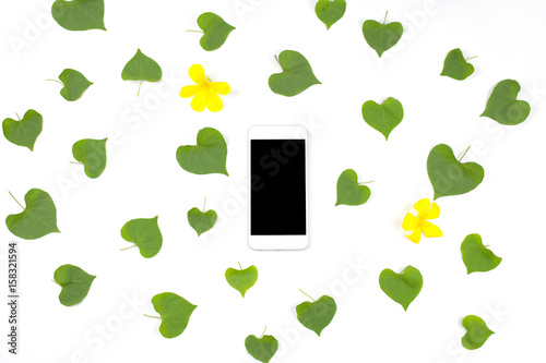 Smart phone with heart shape leaves and yellow flowers on white background. flat lay.