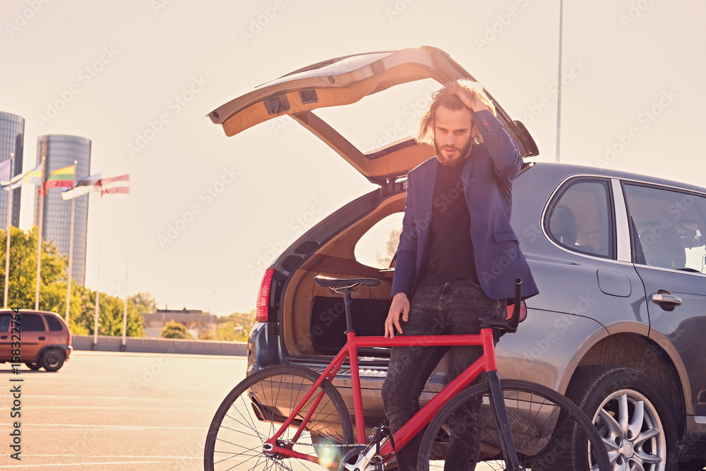 Naklejka premium A man holds fixed bicycle near the car with open trunk.