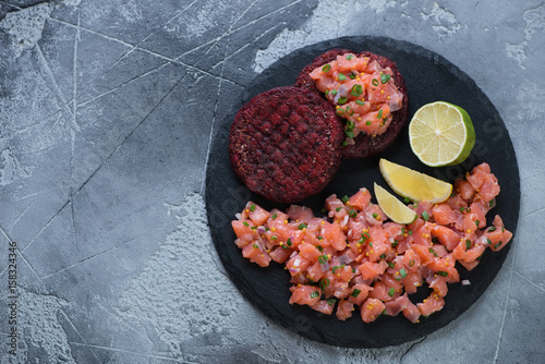 Stone slate with salmon tartar and beetroot cutlets. Flat-lay on a grey stone background with copyspace, horizontal shot