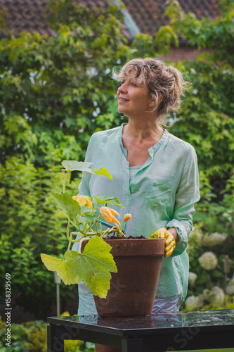 Attractive woman processes vegetable  in her garden looking up.