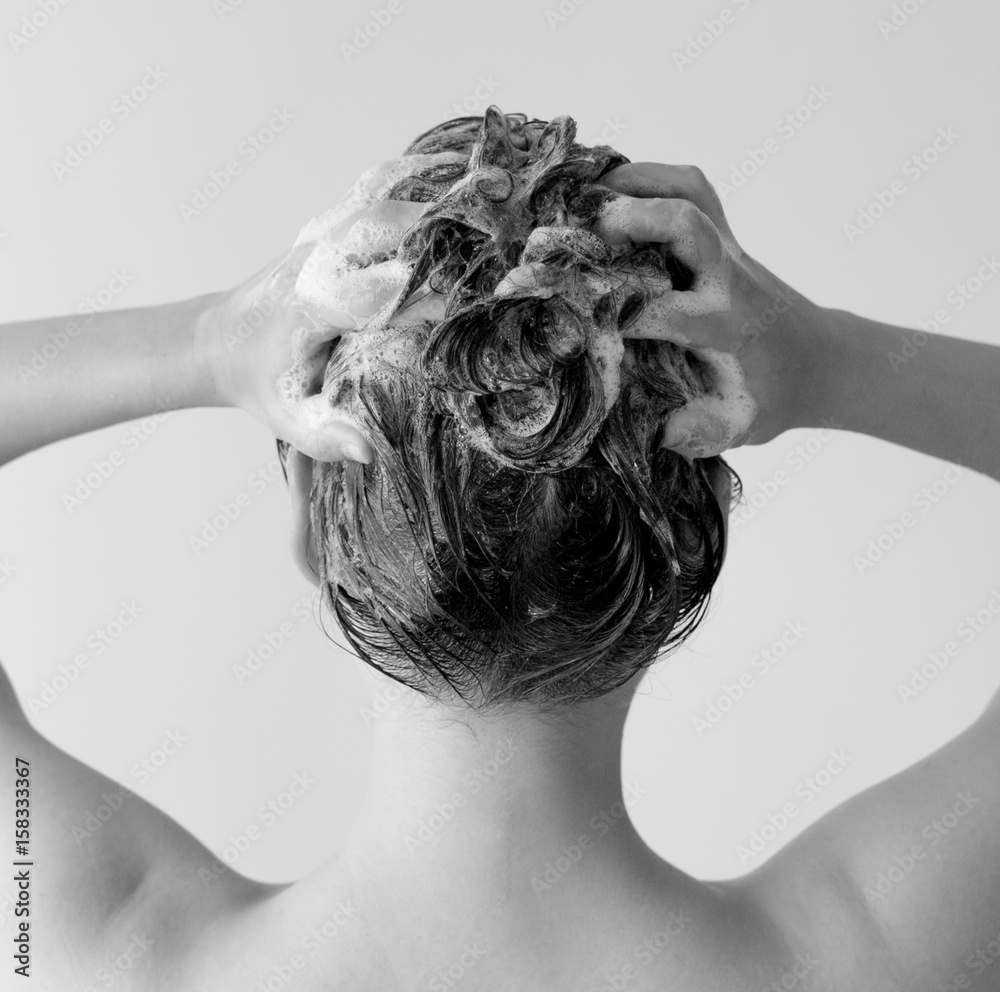 Φωτογραφία Back of a woman in a shower shampooing her hair, massaging her head full of suds in black and white