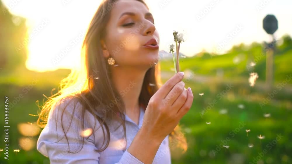 Beauty woman blowing dandelion against the sunset, slow motion Beauty woman blowing dandelion against the sunset, slow motion