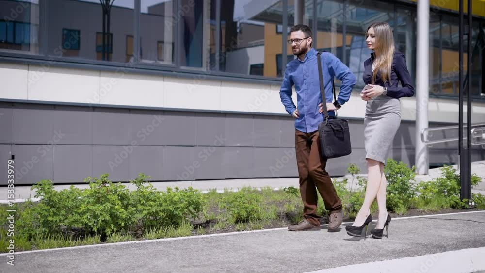 Colleagues on work stroll near the building of the form on their lunch break, they go towards the office to continue their work Colleagues on work stroll near the building of the form on their lunch break, they go towards the office to continue their work