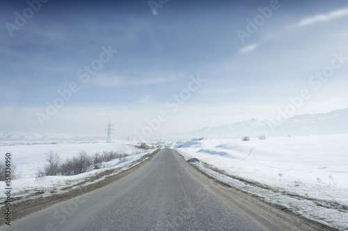 Winter sunny road to mountains at the blue skyline with a lot of snow everywhere