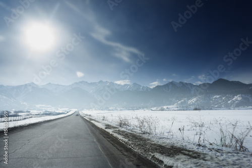 Winter sunny road to mountains at the blue skyline with a lot of snow everywhere photo