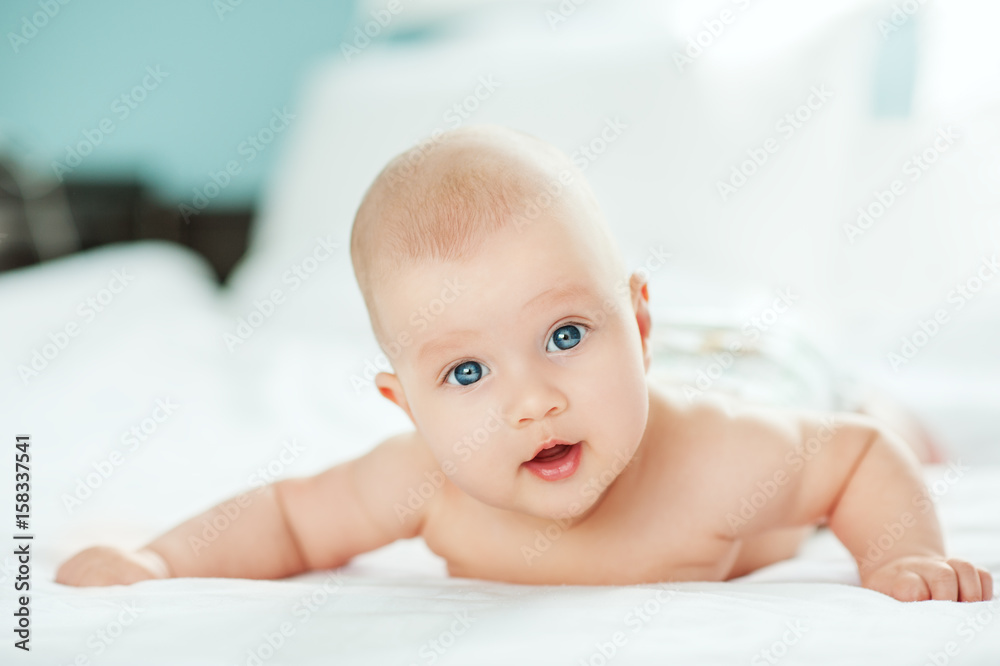 Adorable baby girl in white sunny bedroom. Newborn child relaxing and laying on belly on bed. Nursery for young children. Textile for kids. Family morning at home. Newborn kid during tummy time. Adorable baby girl in white sunny bedroom. Newborn child relaxing and laying on belly on bed. Nursery for young children. Textile for kids. Family morning at home. Newborn kid during tummy time.