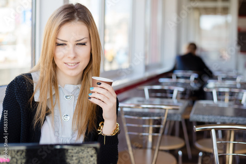 Pretty woman with hands holding coffee cup and working on laptop over restaurant background, mockup space for text message or design. closeup portrait